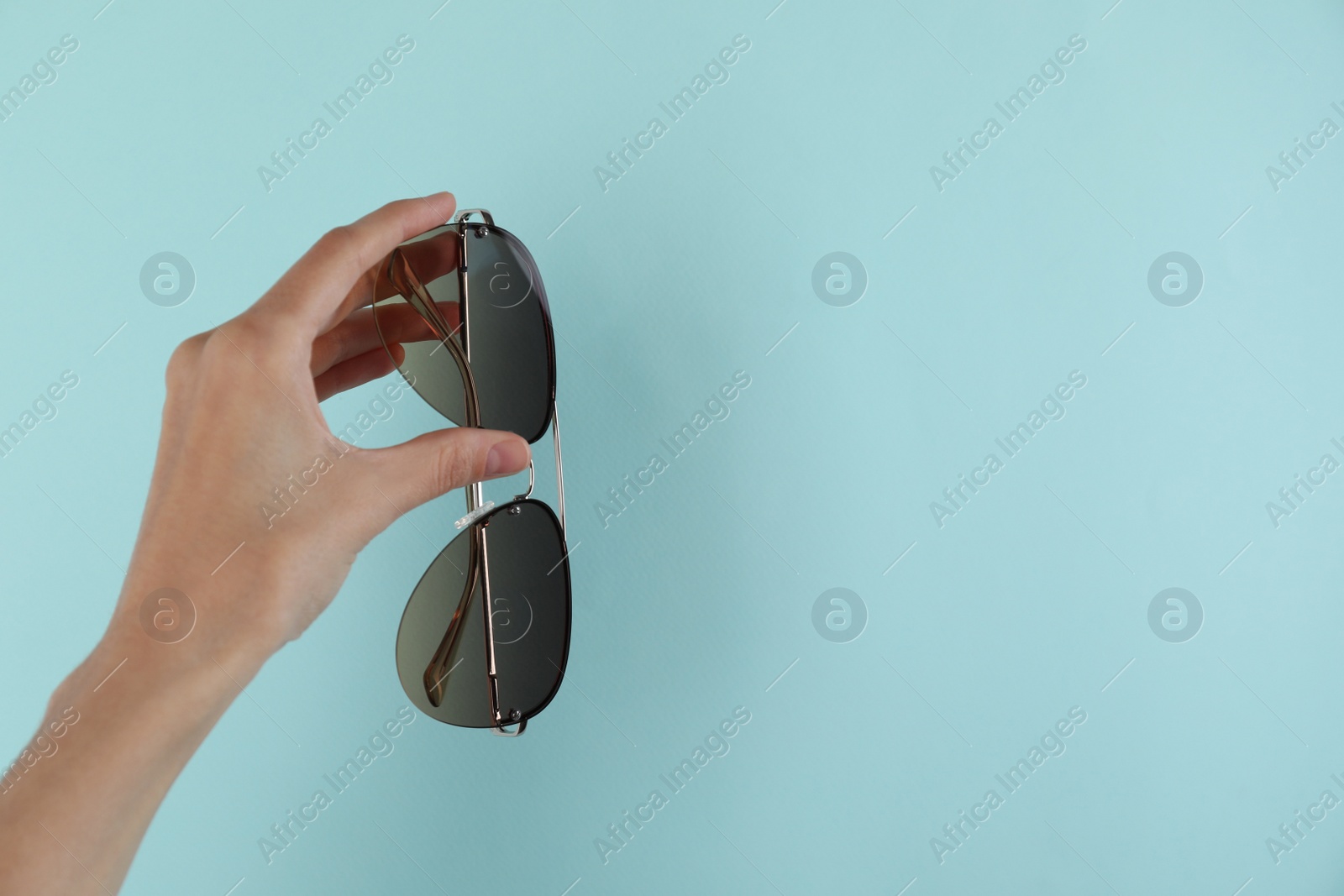 Photo of Woman holding stylish sunglasses on light blue background, closeup. Space for text