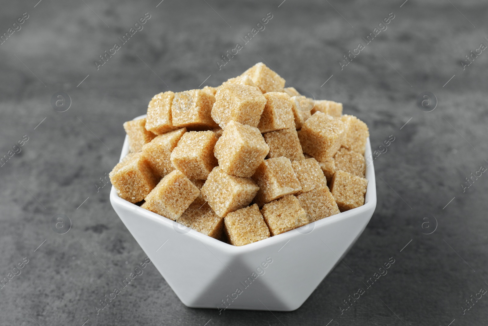 Photo of Brown sugar cubes in bowl on grey table