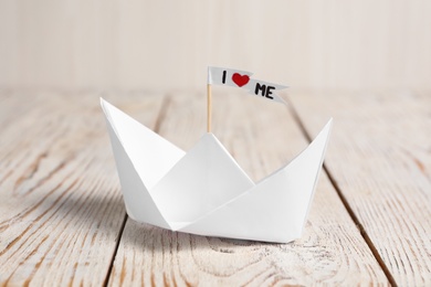 Photo of Paper ship and flag with phrase I Love Me on wooden table