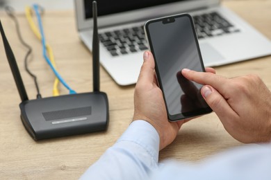 Photo of Man with smartphone and laptop connecting to internet via Wi-Fi router at wooden table, closeup