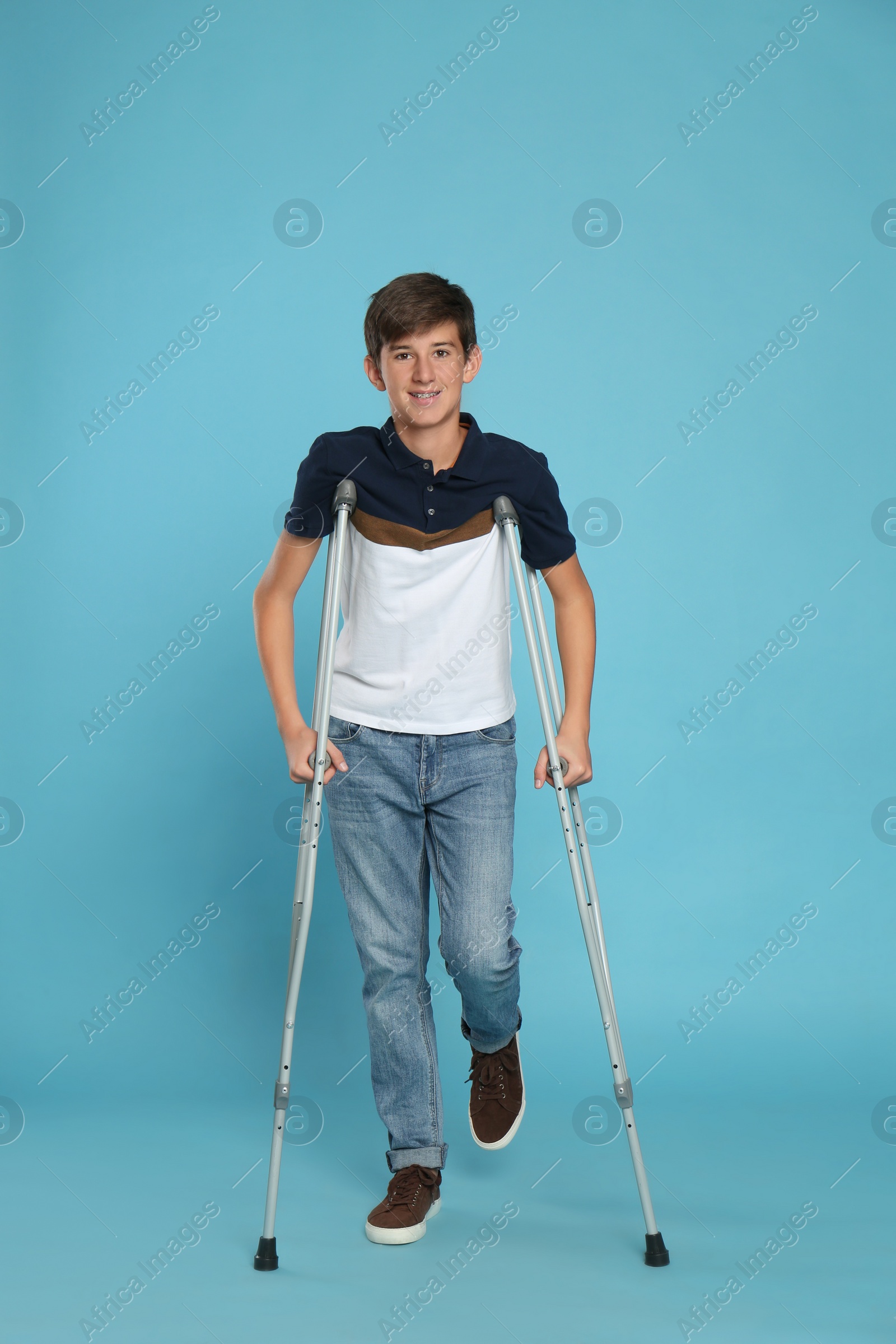 Photo of Teenage boy with injured leg using crutches on turquoise background