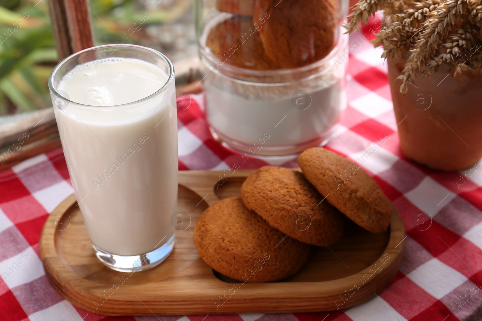 Photo of Glass of milk with cookies on red checkered tablecloth indoors