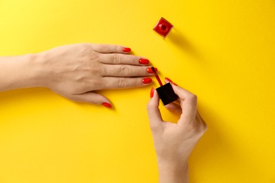Photo of Woman applying bright nail polish on color background, top view