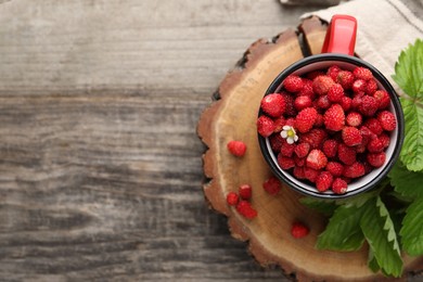 Photo of Fresh wild strawberries in mug and leaves on wooden table, top view. Space for text