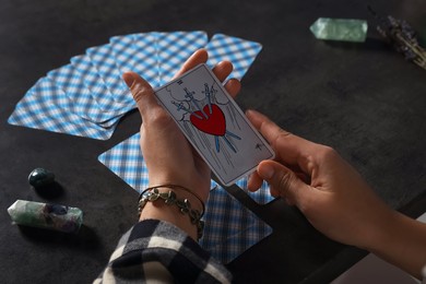 Fortune teller with tarot card Three of Swords at grey table, closeup