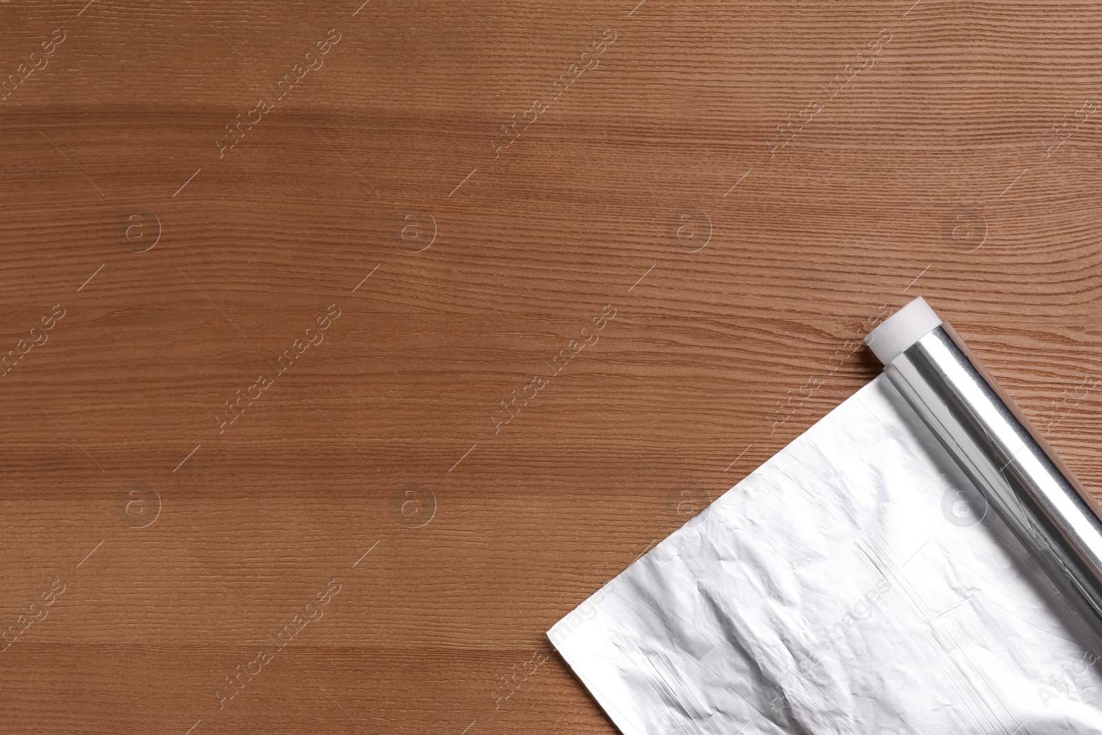 Photo of Roll of aluminum foil on wooden table, top view. Space for text