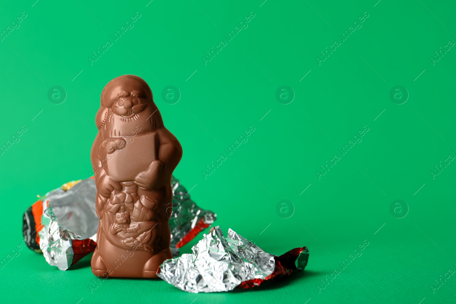 Photo of Unwrapped chocolate Santa Claus on green background. Space for text