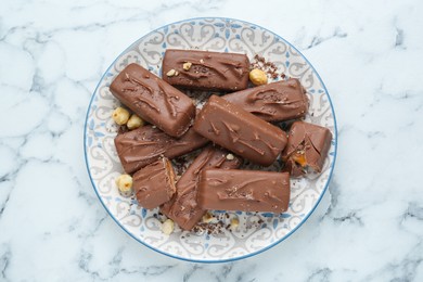 Photo of Delicious chocolate candy bars with nuts on white marble table, top view