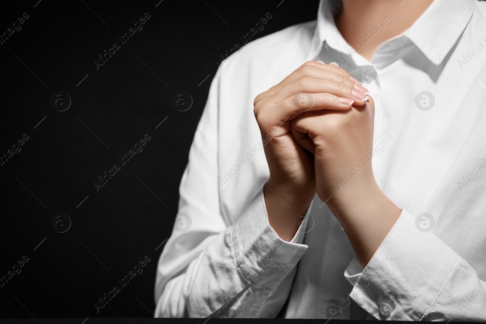 Photo of Woman holding hands clasped while praying against black background, closeup. Space for text