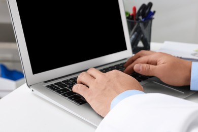 Doctor working with laptop at white desk in clinic, closeup. Online medicine