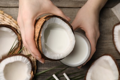 Woman holding tasty coconut near glass with vegan milk at wooden table, closeup