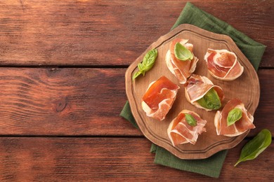 Photo of Board of tasty sandwiches with cured ham and basil leaves on wooden table, top view. Space for text