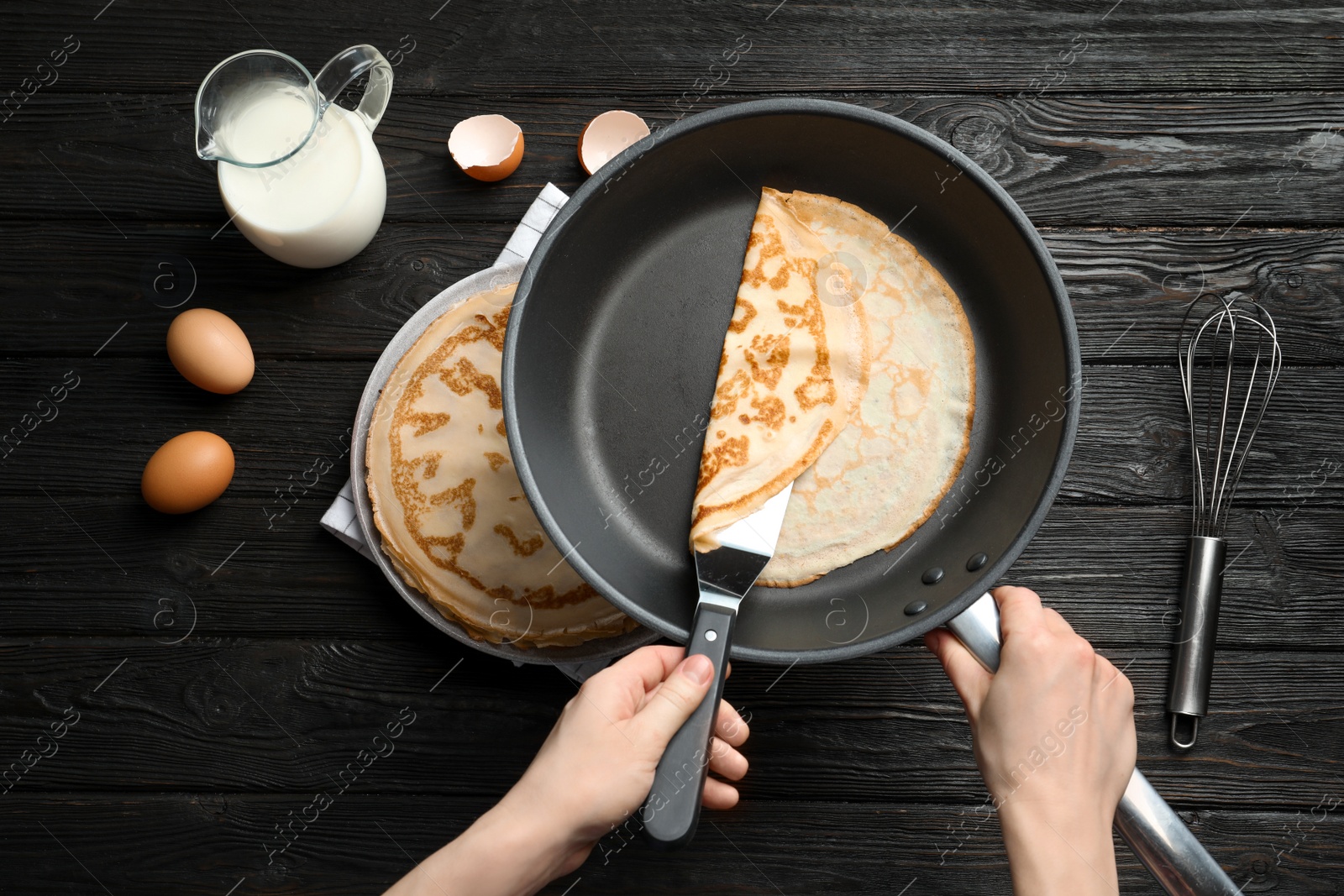 Photo of Woman holding frying pan with thin pancake over table, top view