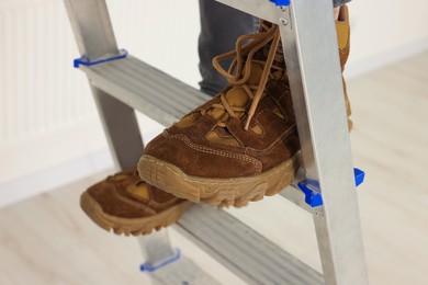 Man climbing up metal stepladder near white wall indoors closeup. Room renovation