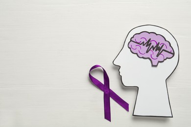 Photo of Human head cutout, brain and purple ribbon on white wooden background, flat lay with space for text. Epilepsy awareness
