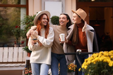 Photo of Happy friends with paper cups of coffee near cafe outdoors