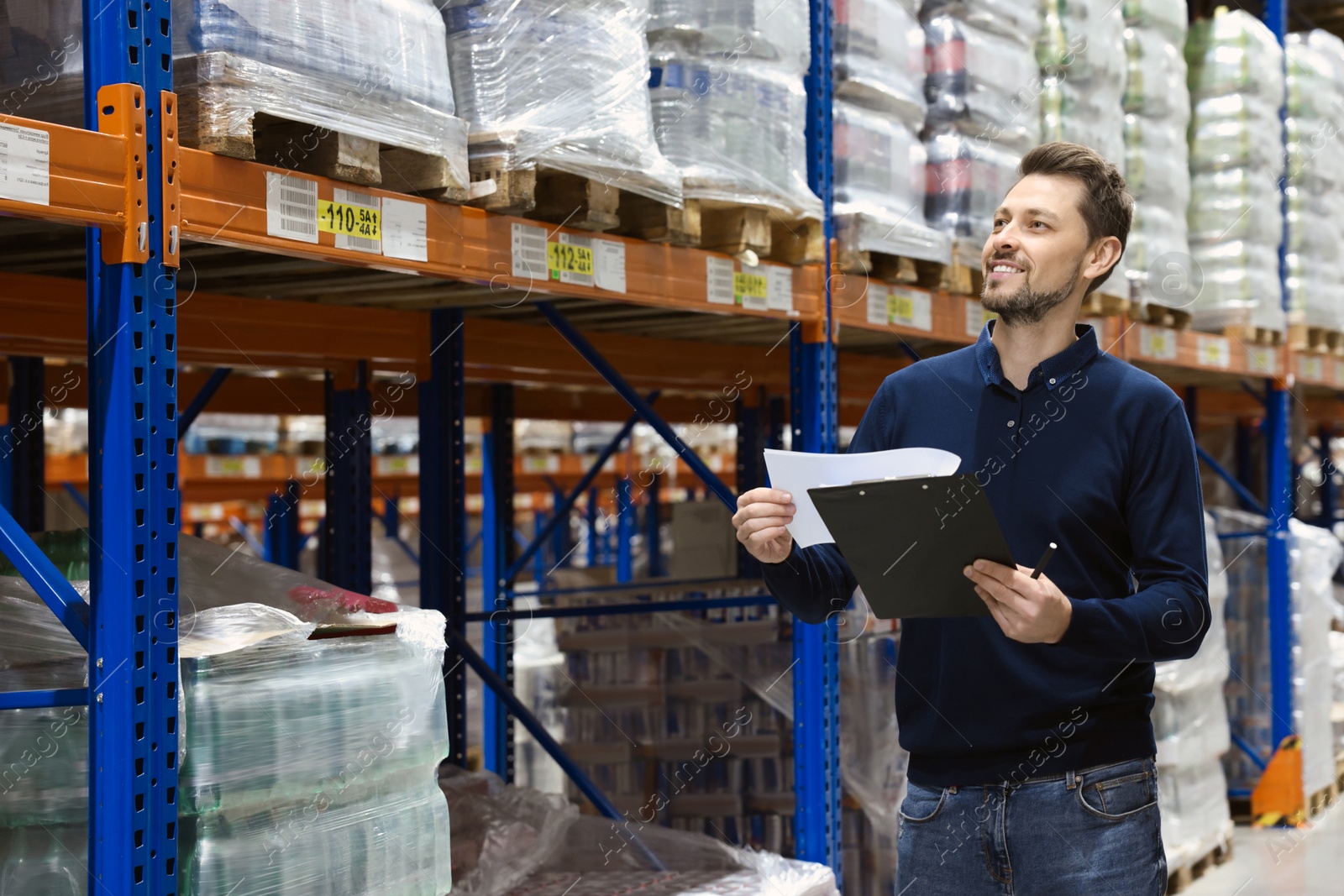 Photo of Happy manager holding clipboard in warehouse with lots of products