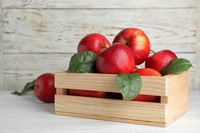 Photo of Juicy red apples in wooden crate on table