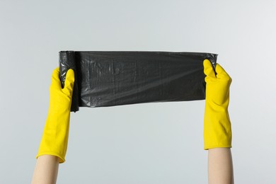 Photo of Janitor in rubber gloves holding roll of black garbage bags on light grey background, closeup