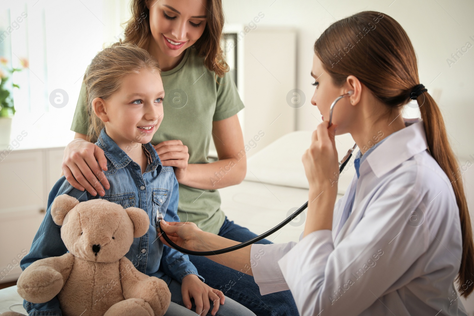 Photo of Mother and daughter visiting pediatrician. Doctor examining little patient with stethoscope in hospital