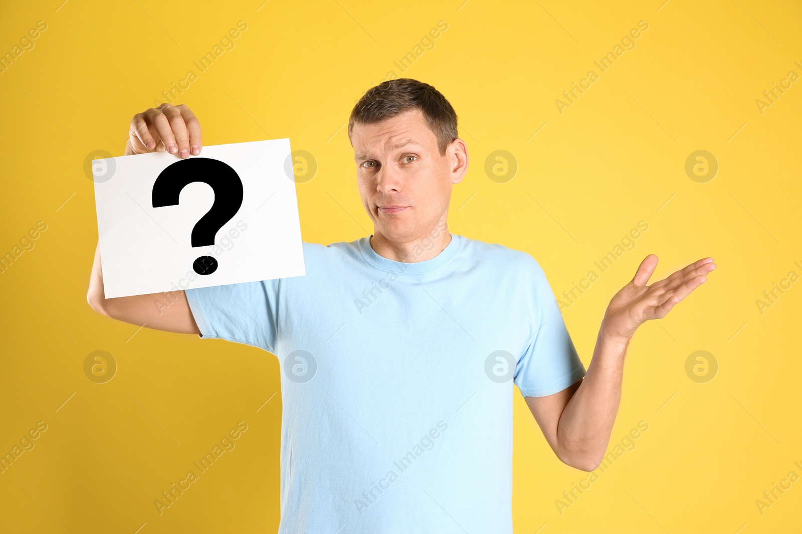 Photo of Emotional man holding paper with question mark on yellow background