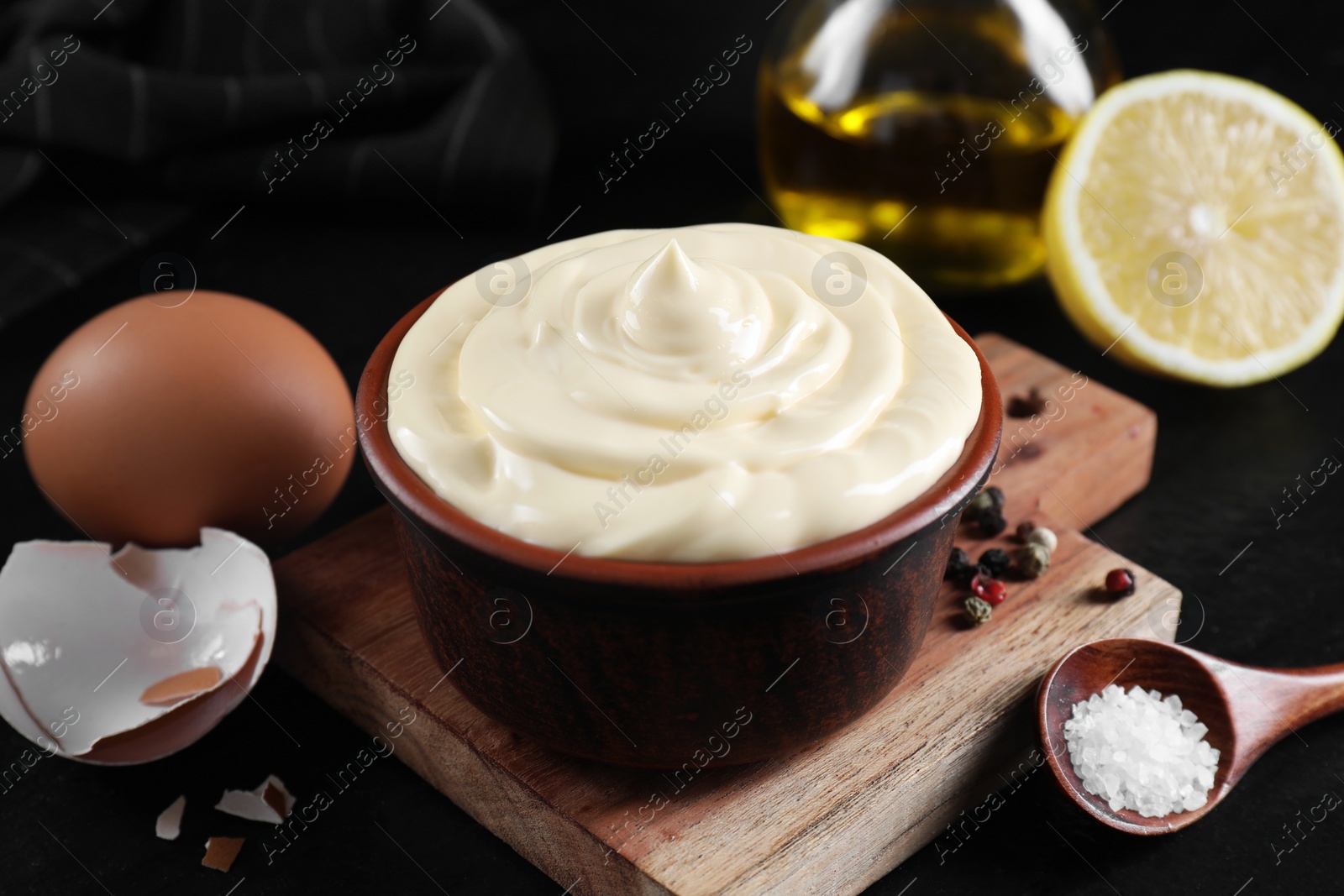 Photo of Fresh mayonnaise sauce in bowl and ingredients on black table, closeup