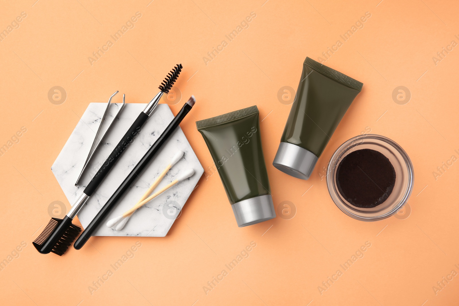 Photo of Flat lay composition with eyebrow henna, professional tools and cosmetic products on orange background