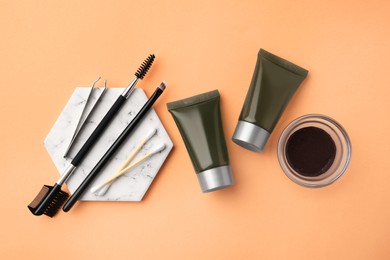 Photo of Flat lay composition with eyebrow henna, professional tools and cosmetic products on orange background