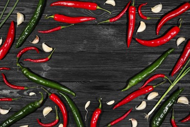 Photo of Frame of different chili peppers and garlic on black wooden table, flat lay. Space for text