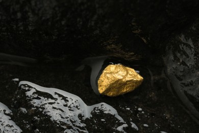Shiny gold nugget on wet stone, top view. Space for text