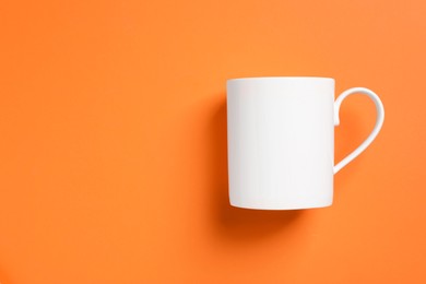 Photo of One white ceramic mug on orange background, top view. Space for text