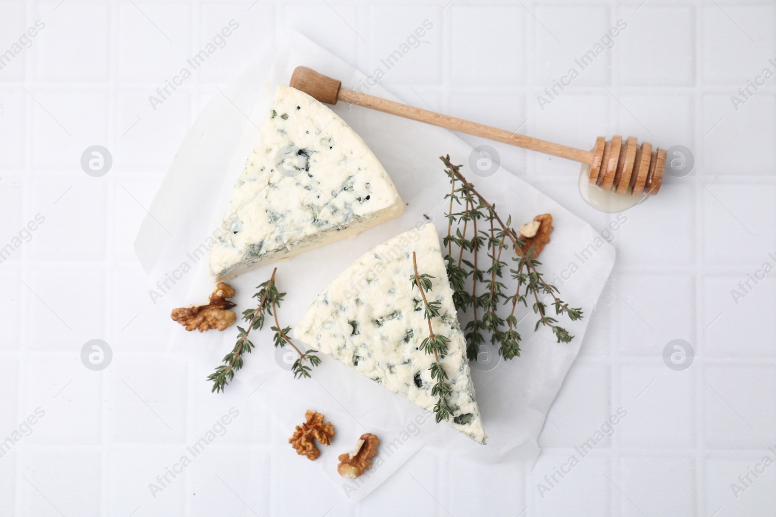 Photo of Tasty blue cheese with thyme, walnuts and honey dipper on white tiled table, flat lay