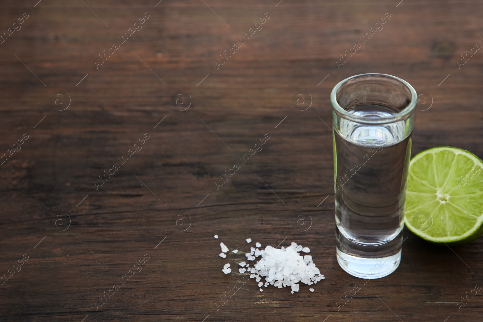 Photo of Mexican tequila shots with lime and salt on wooden table. Space for text