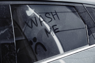 Inscription WASH ME and sad smiley on car window, closeup