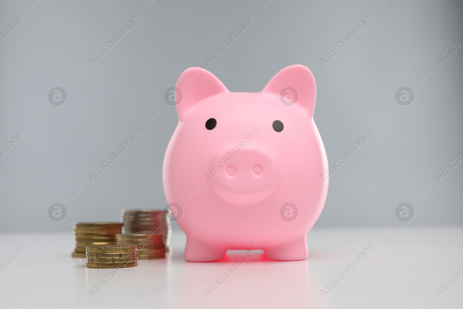 Photo of Pink piggy bank and coins on white table