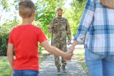 Photo of Little boy with mother meeting his father in military uniform outdoors