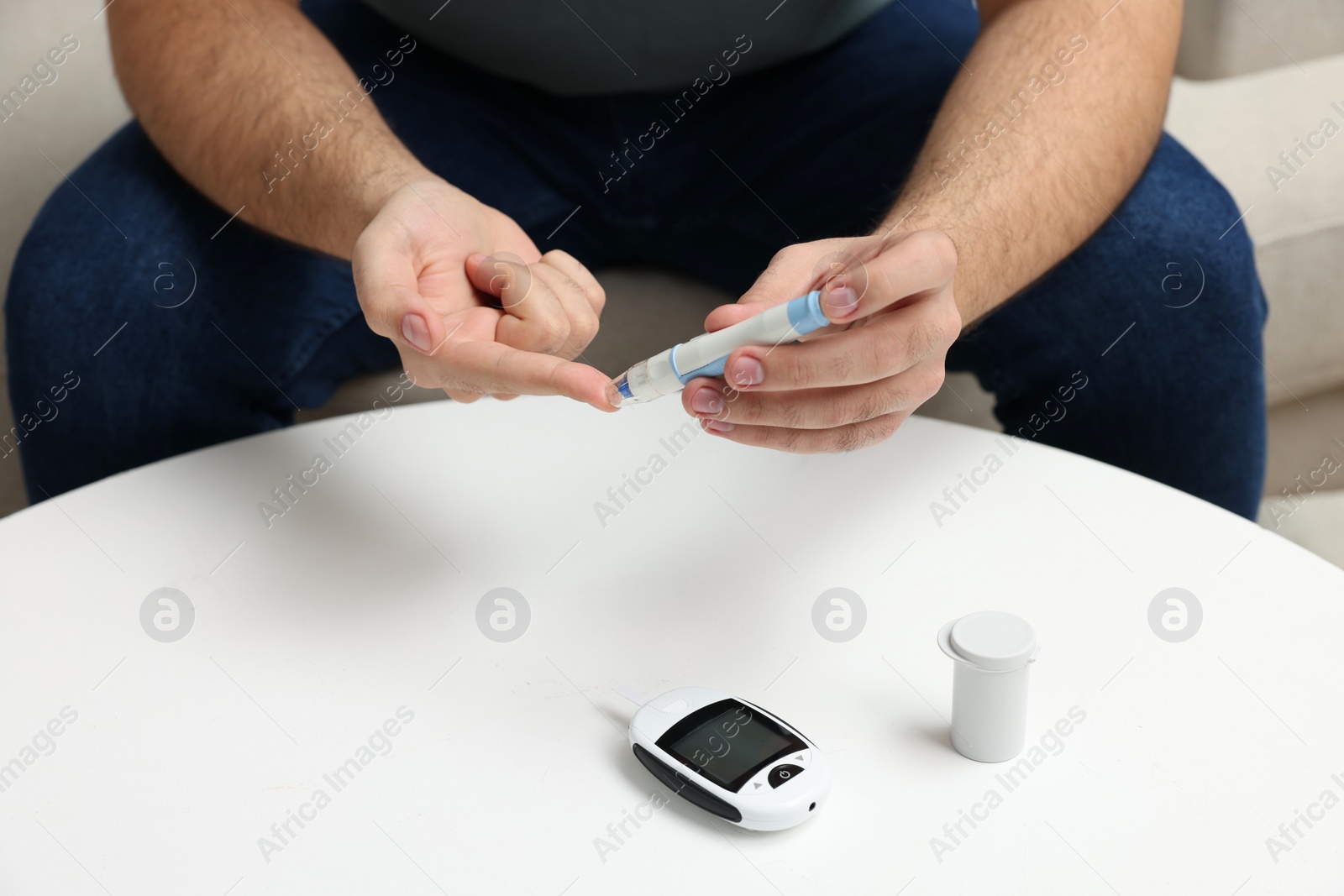 Photo of Diabetes test. Man checking blood sugar level with lancet pen at white table, closeup