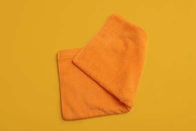 Photo of Folded orange beach towel on yellow background, top view