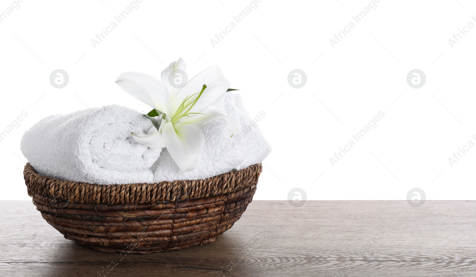 Photo of Fresh towels and lily flower on wooden table against white background. Space for text