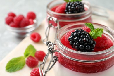 Photo of Delicious panna cotta with fruit coulis and fresh berries in glass jars, closeup