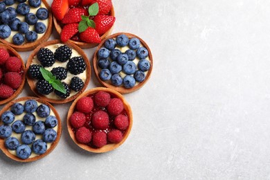 Photo of Tartlets with different fresh berries on light table, flat lay and space for text. Delicious dessert