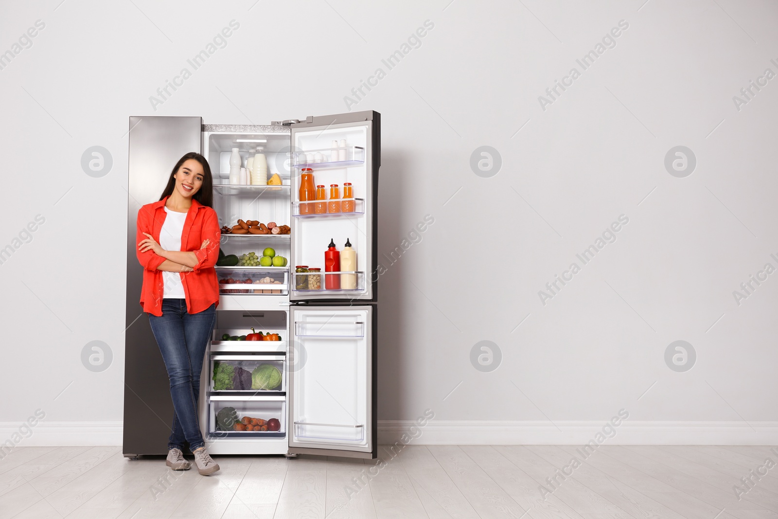 Photo of Happy young woman near open refrigerator indoors, space for text