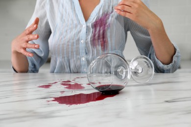 Photo of Woman with spilled glass of wine and stain on her shirt at table indoors, closeup