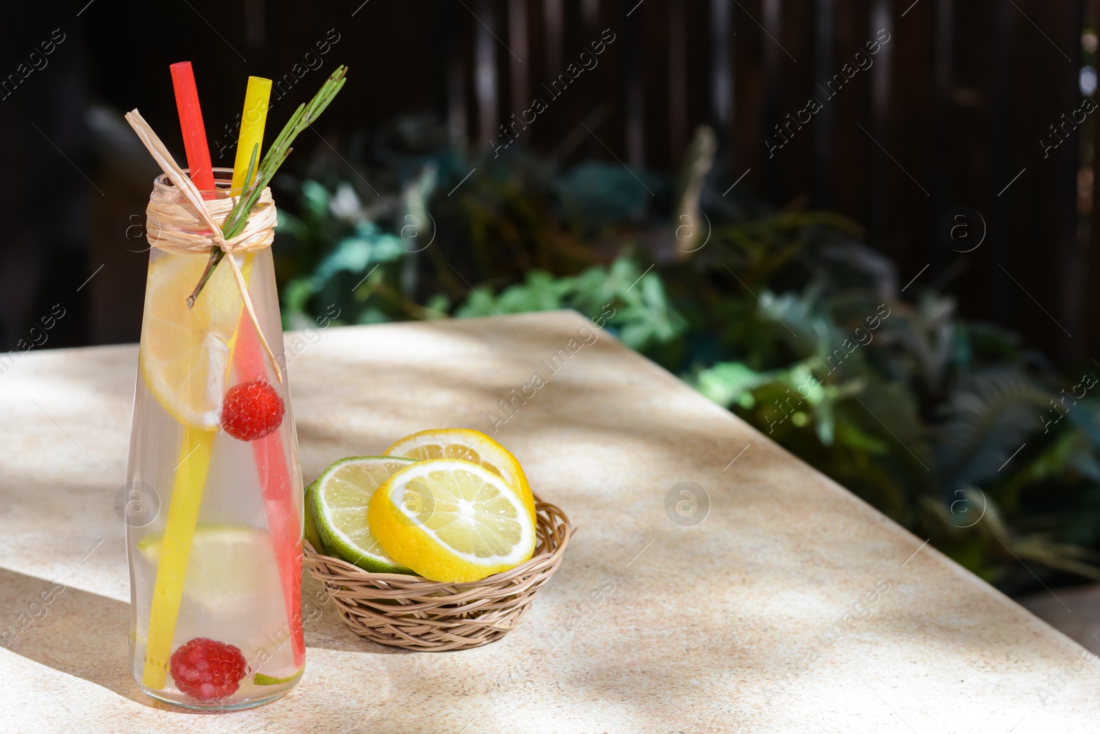 Photo of Refreshing tasty lemonade served in glass bottle and citrus fruits on beige table. Space for text