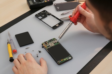 Photo of Technician repairing broken smartphone at table, closeup