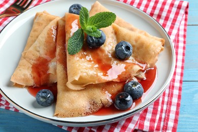 Delicious crepes served with blueberries, mint and syrup on table, closeup