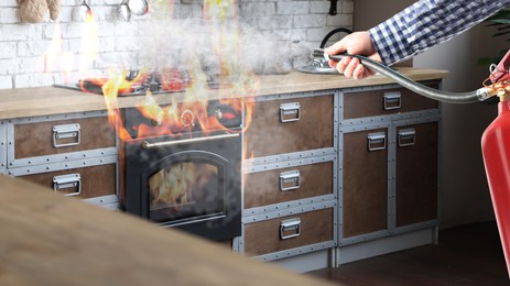 Man putting out burning stove and oven with fire extinguisher in kitchen, closeup