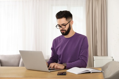 Photo of Handsome young man working with laptop at table in home office
