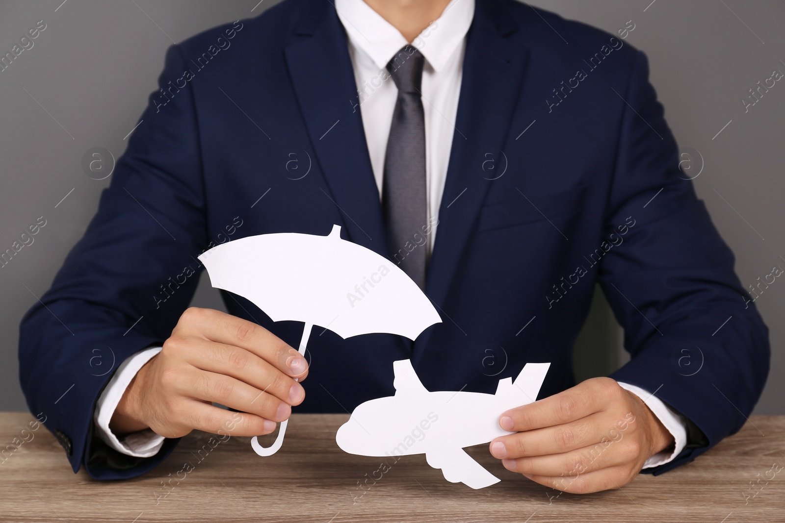 Photo of Insurance agent covering paper plane with umbrella cutout at table, closeup. Travel safety concept