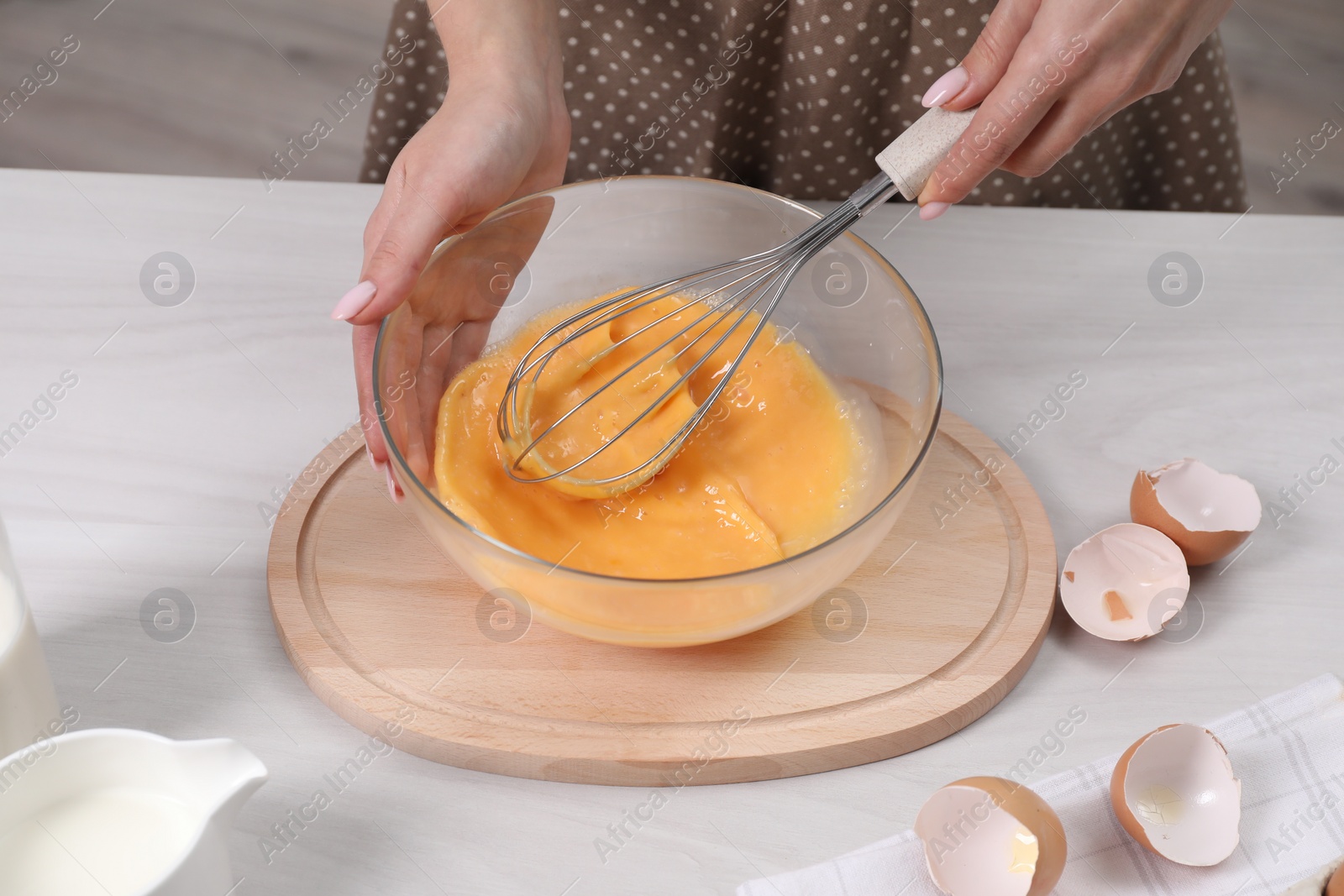 Photo of Woman whisking eggs in bowl at table indoors, closeup